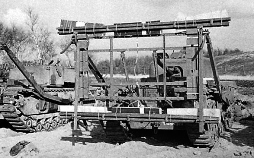 Front view of a Churchill Mark IV tank, of The Calgary Regiment, at Whitley, Surrey, fitted with the “Onion” explosive device. In this case, the high explosive charges in boxes are attached three along the top and three along the bottom of the outer face of the framework. Note also, the two outward facing legs, attached to either corner of the top of the framework, which would enable the device to be hung from an obstacle such as a wall or bunker. Source: MilArt photo archive. 